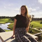 Audrey Kohrnak sitting on a railing in front of a golf course